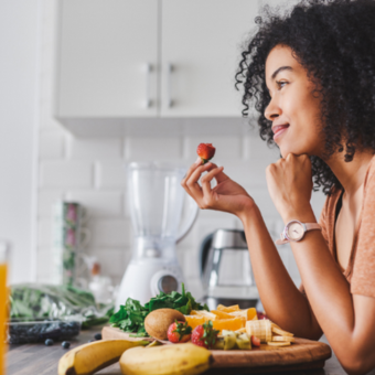 A woman sitting in a kitchen eating fruit with some juice in the foreground