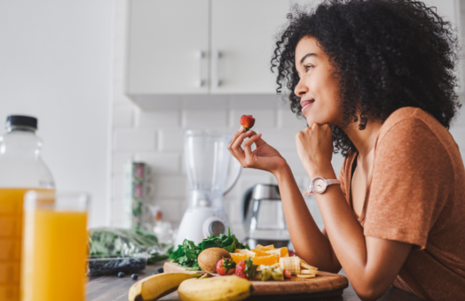 A woman sitting in a kitchen eating fruit with some juice in the foreground