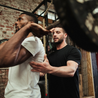 A personal trainer assisting a man weight lifting in a gym