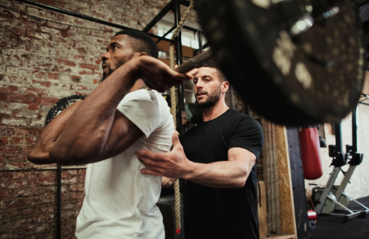 A personal trainer assisting a man weight lifting in a gym