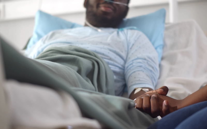 man in hospital bed holding hands with a relative